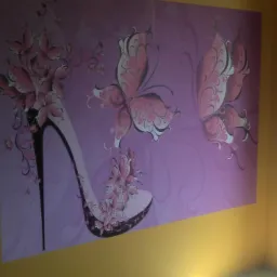 Różowa tapeta z motywem buta na wysokim obcasie i motyli, na żółtej ścianie w rogu pokoju.