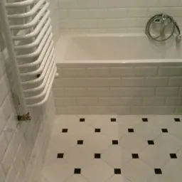 Biała łazienka z wanną obłożoną kafelkami typu metro, grzejnikiem drabinkowym i podłogą w biało-czarną szachownicę.