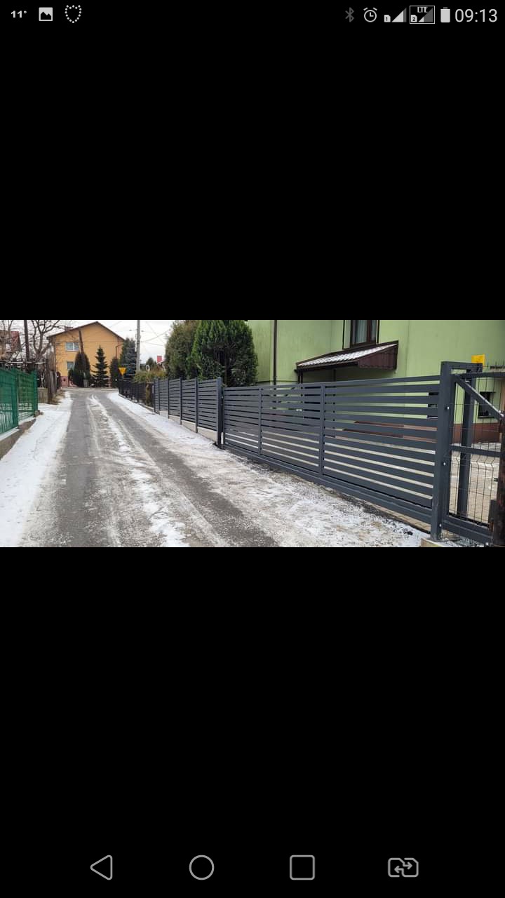 Nowoczesne, poziome ogrodzenie panelowe w kolorze grafitowym z bramą przesuwną, widoczne z perspektywy ulicy pokrytej śniegiem w zimowy dzień.