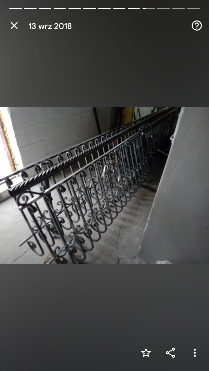 Elementy metalowej balustrady z dekoracyjnymi motywami, przygotowane do montażu, leżące w pomieszczeniu.