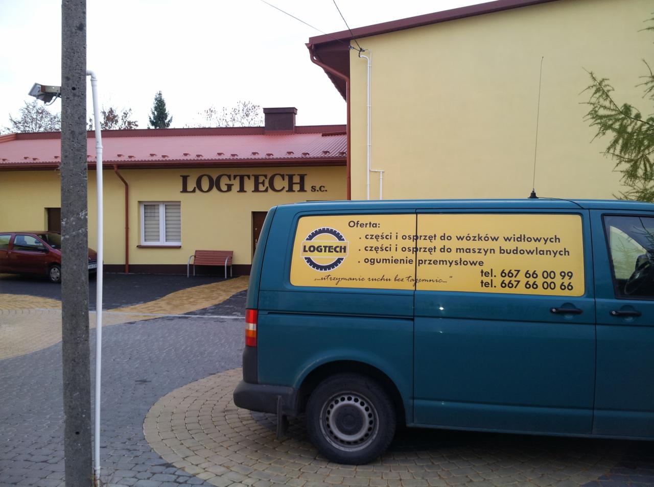 Błękitny samochód dostawczy z reklamą firmy Logtech S.C. oferującej części i osprzęt do wózków widłowych i maszyn budowlanych, zaparkowany przed budynkiem firmy z żółtą elewacją i czerwonym dachem.