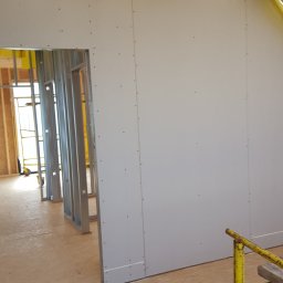 Styldom - Wnętrze w trakcie montażu płyt karton-gips na metalowym stelażu. Widoczne drewniane elementy konstrukcji dachu i żółta folia zabezpieczająca.