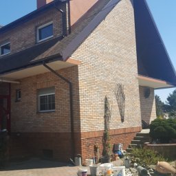 Styldom - Dom z cegły klinkierowej po renowacji elewacji, widoczny fragment dachu, komin i teren wokół domu z materiałami budowlanymi.