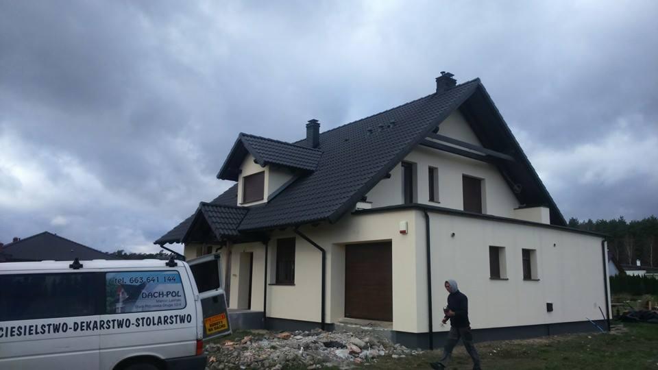 Dom jednorodzinny w Śmiglu z nowym, ciemnoszarym dachem z dachówki ceramicznej, widok z boku, na pierwszym planie częściowo widoczny samochód dostawczy z reklamą firmy dekarskiej.