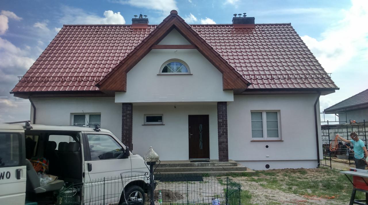 Nowy dom jednorodzinny z dwuspadowym dachem pokrytym czerwoną dachówką, widok z przodu z samochodem dostawczym zaparkowanym obok.