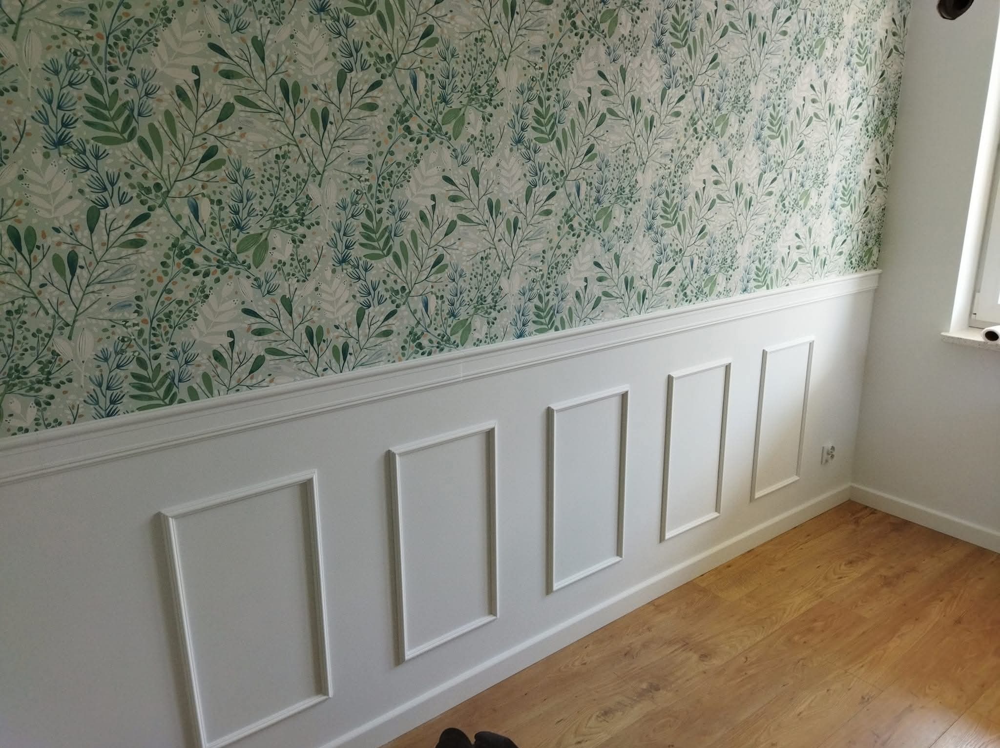 Ściana z dekoracyjną boazerią w stylu angielskim i tapetą w roślinny wzór. Parkiet na podłodze. Wykończenie wnętrza w jasnych kolorach.