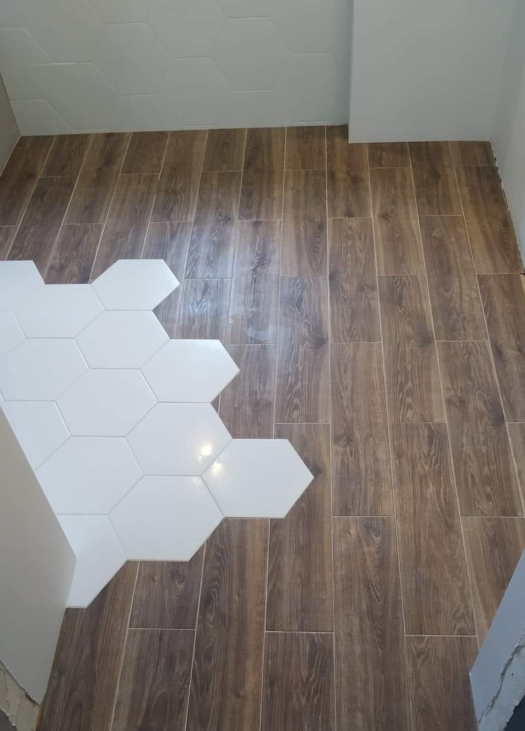 Ułożona podłoga z płytek imitujących drewno, z fragmentem białych, heksagonalnych płytek. Widok z góry, ukazujący wzór i fakturę materiałów.