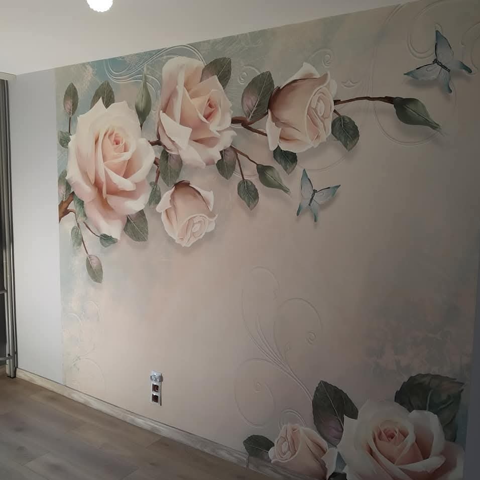 Fototapeta z motywem róż i motyli na ścianie w pokoju, widoczny fragment podłogi i gniazdko elektryczne. Dekoracja wnętrza w pastelowych barwach.