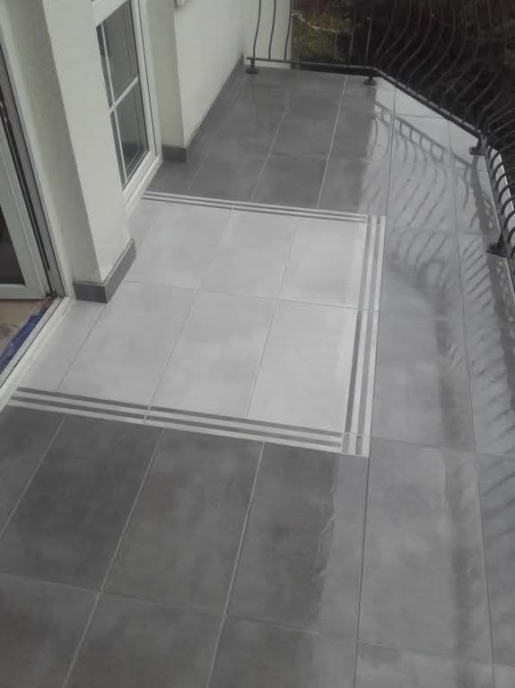 Wykończony balkon z szarymi i białymi płytkami, wzór obramowania. Widoczne balustrady i okno balkonowe. Nowoczesny design z połyskiem na płytkach.