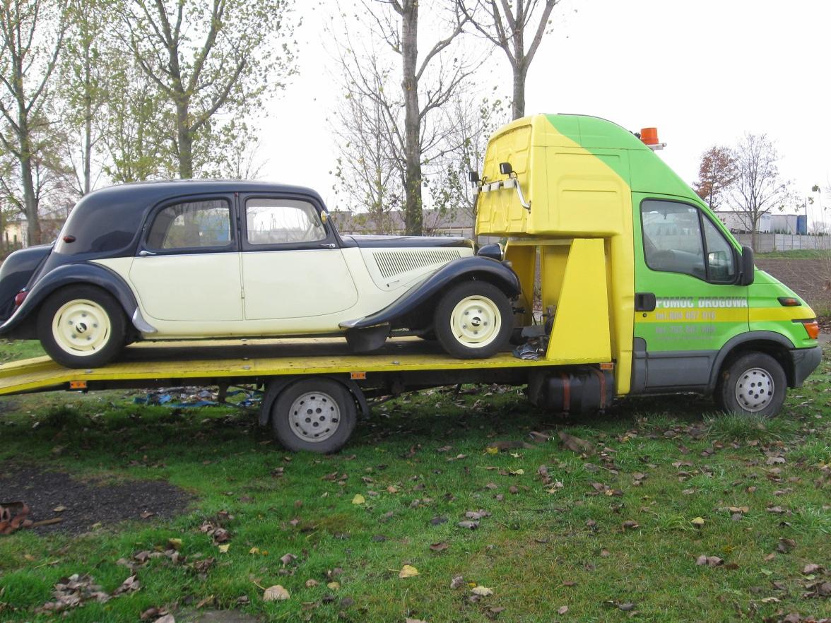 Laweta w kolorach żółto-zielonych przewozi zabytkowy samochód Citroen Traction Avant na żółtej platformie. Widoczny napis 'Pomoc Drogowa' na kabinie lawety.