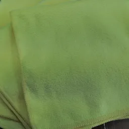 Jasnożółte, złożone ściereczki z mikrofibry na drewnianym blacie, widoczna faktura materiału i szew na krawędzi