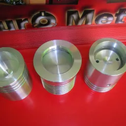 Precyzyjnie obrobione, metalowe elementy cylindryczne na czerwonym tle, z widocznymi śladami toczenia i otworami, prezentowane jako przykład obróbki CNC lub tokarskiej.