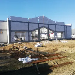 Wznoszenie ścian budynku z betonu komórkowego w Sierakowicach, widoczne rusztowania i zbrojenia, teren budowy w trakcie prac.