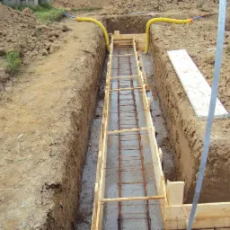 Wykop pod fundamenty z szalunkiem i zbrojeniem w Rokowie, widoczne żółte rury doprowadzające media.