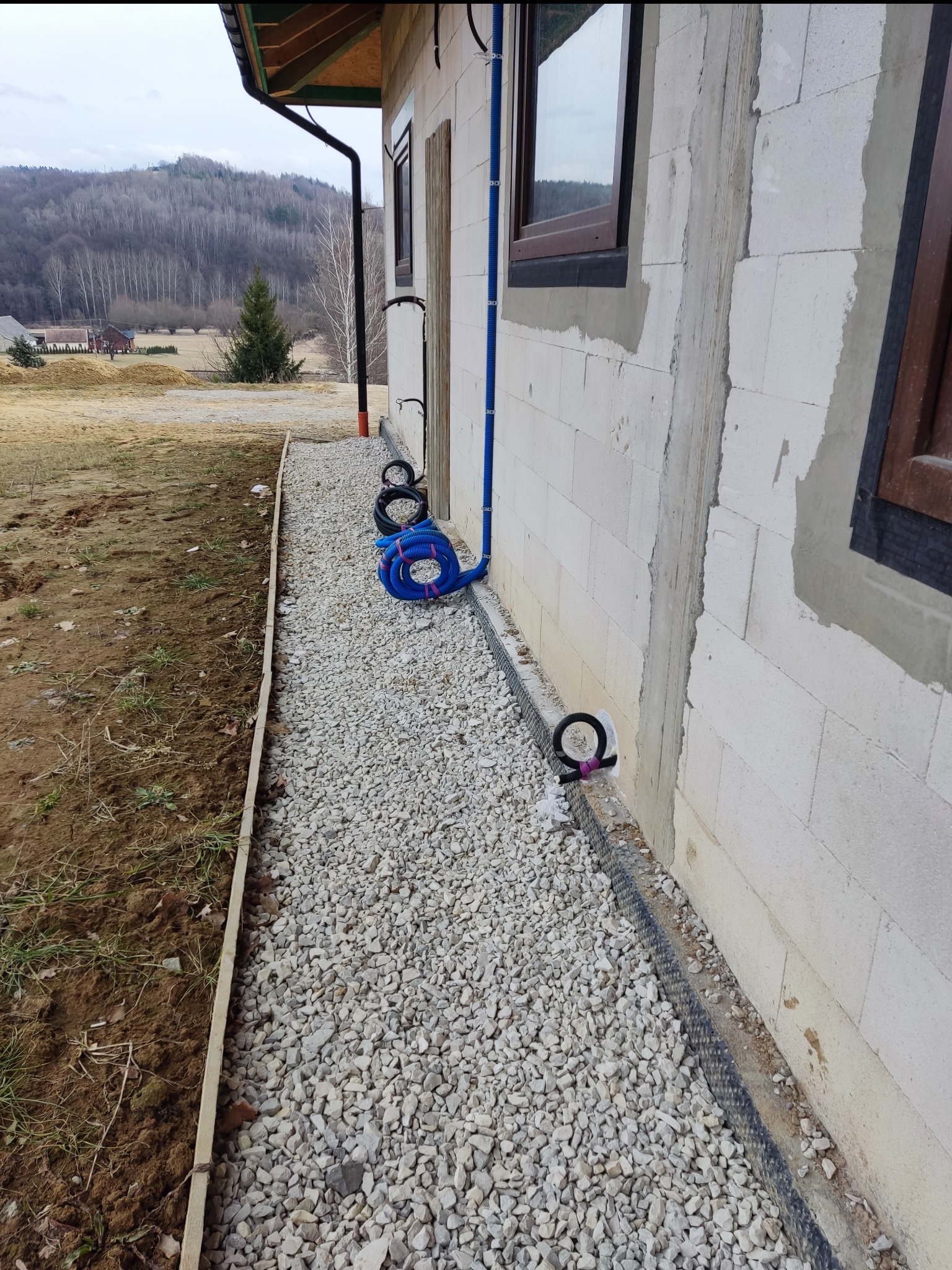 Instalacja elektryczna w Polichtach: niebieskie rury prowadzone po elewacji budynku z betonu komórkowego, widoczne elementy mocujące i peszle.