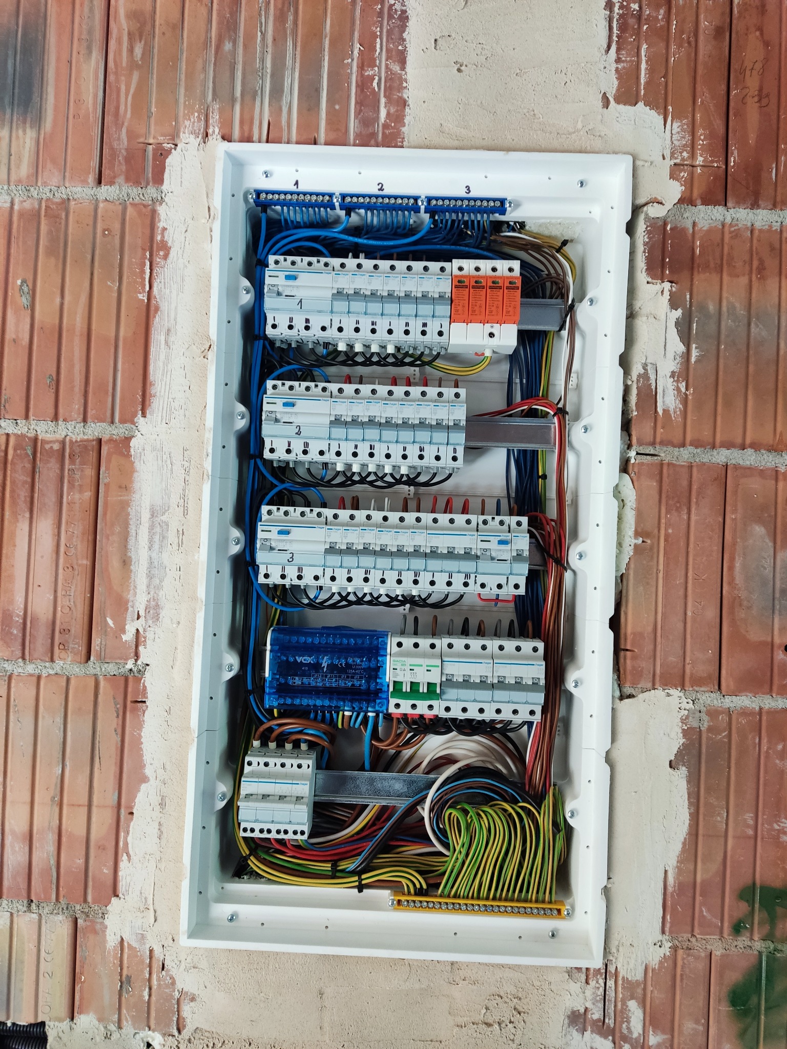 Rozdzielnica elektryczna z zabezpieczeniami, zamontowana w ścianie z cegły. Widoczne przewody i aparatura modułowa.