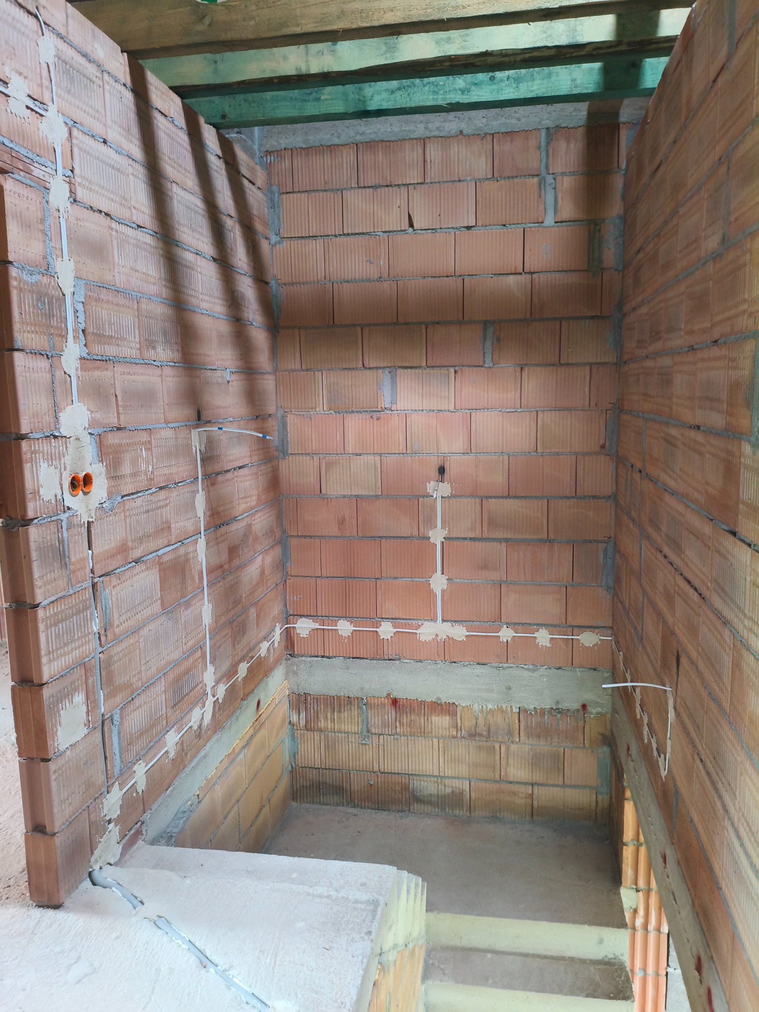 Instalacja przewodów elektrycznych w nowym budynku z cegły w Polichtach. Widoczne puszki i kable przymocowane do ściany, przygotowane do dalszych prac.