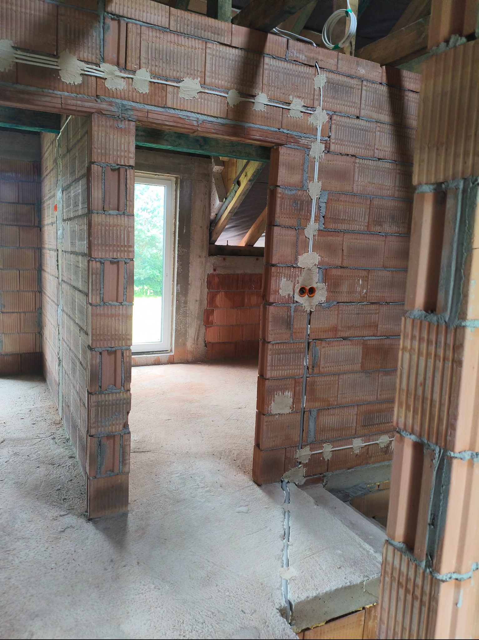 Wewnętrzne mury z pustaków ceramicznych w trakcie montażu instalacji elektrycznej. Widoczne kable i puszki elektryczne. Surowy stan budynku przed wykończeniem.