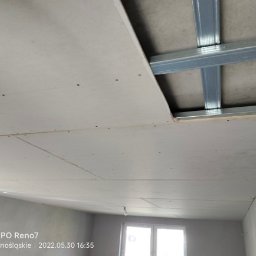 Usługi remontowe Gopus - Widok na sufit w trakcie montażu, widoczne metalowe profile konstrukcyjne i częściowo zamontowane płyty, z widocznymi śladami po wkrętach.