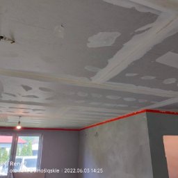 Usługi remontowe Gopus - Płyta karton gips na suficie w trakcie szpachlowania, widoczne łączenia płyt, przygotowanie do dalszych prac wykończeniowych, ściany zabezpieczone taśmą malarską.