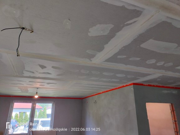 Płyta karton gips na suficie w trakcie szpachlowania, widoczne łączenia płyt, przygotowanie do dalszych prac wykończeniowych, ściany zabezpieczone taśmą malarską.