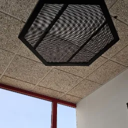 Sufit z płyt drewnopodobnych z sześciokątną lampą rastrową, widok na okno z czerwonymi ramami.