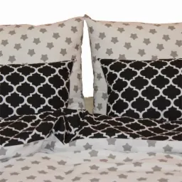 Komplet pościeli: biała kołdra i poduszki w szare gwiazdki, dodatkowe poduszki z czarnym marokańskim wzorem. Widok z bliska, estetyczne ułożenie.