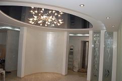 Salon z podwieszanym sufitem o owalnym kształcie, z lustrzanym odbiciem żyrandola. Ściany wykończone w jasnym, kremowym odcieniu z delikatną fakturą. Na pierwszym planie białe, proste kolumny...