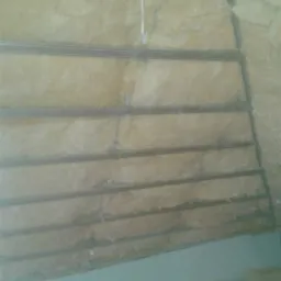 Montaż izolacji z wełny mineralnej między metalowymi profilami na poddaszu, widoczne przewody elektryczne i fragment ściany pomalowanej na jasny kolor.