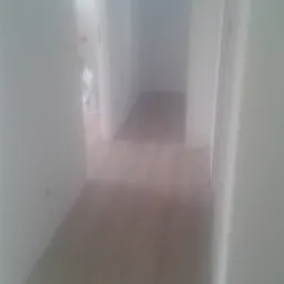 Jasne panele podłogowe w korytarzu z białymi ścianami i framugami drzwi widziane z niskiej perspektywy.