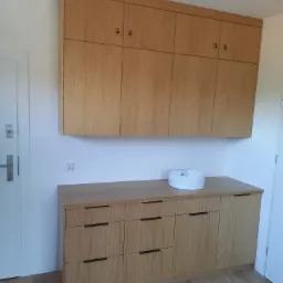 Jasne drewniane szafki wiszące i komoda z umywalką nablatową w Elblągu, minimalistyczny design, widoczne charakterystyczne usłojenie drewna.