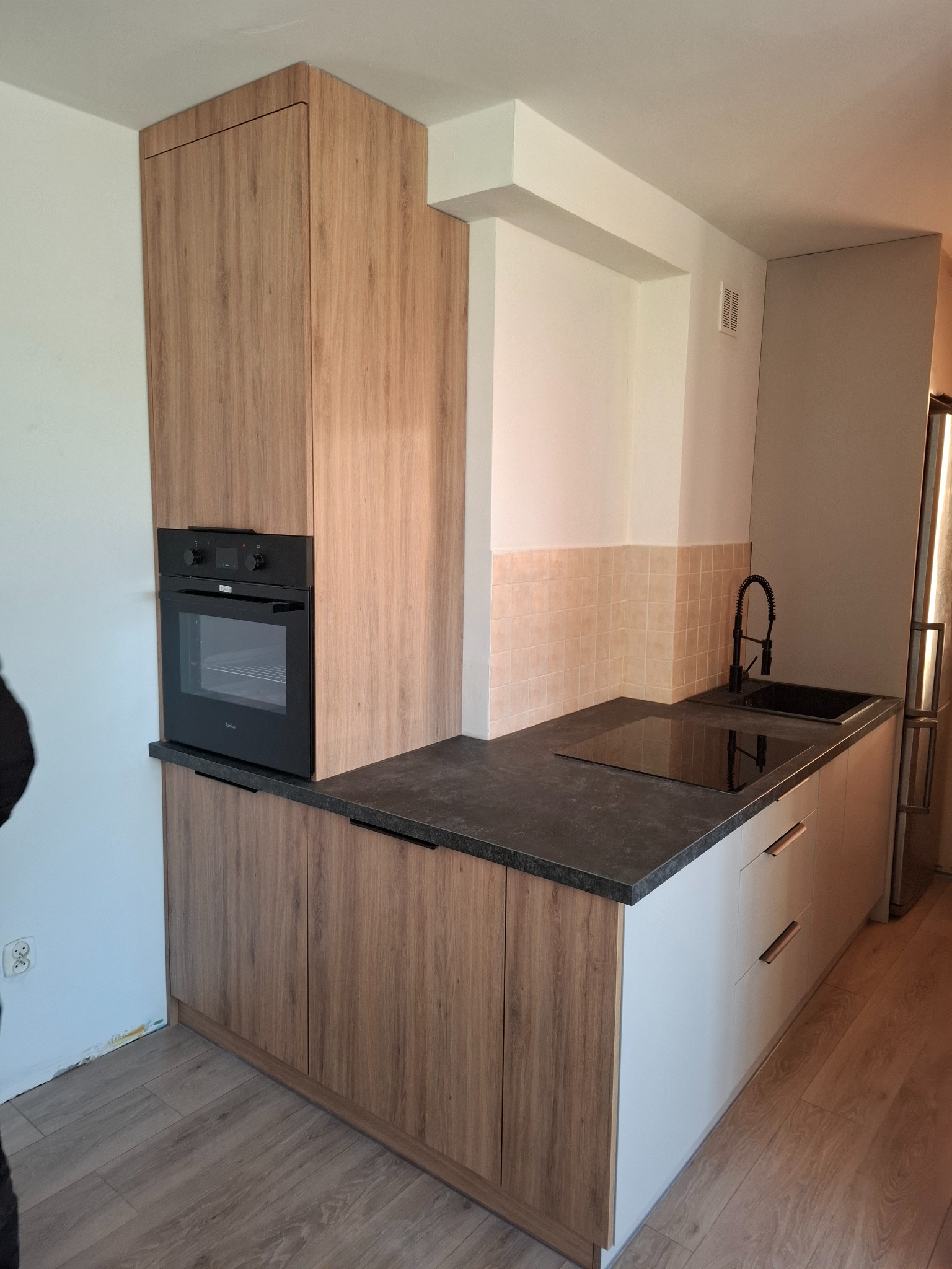 Nowoczesna kuchnia z drewnianymi frontami szafek, czarnym blatem i piekarnikiem w zabudowie, minimalistyczna armatura.