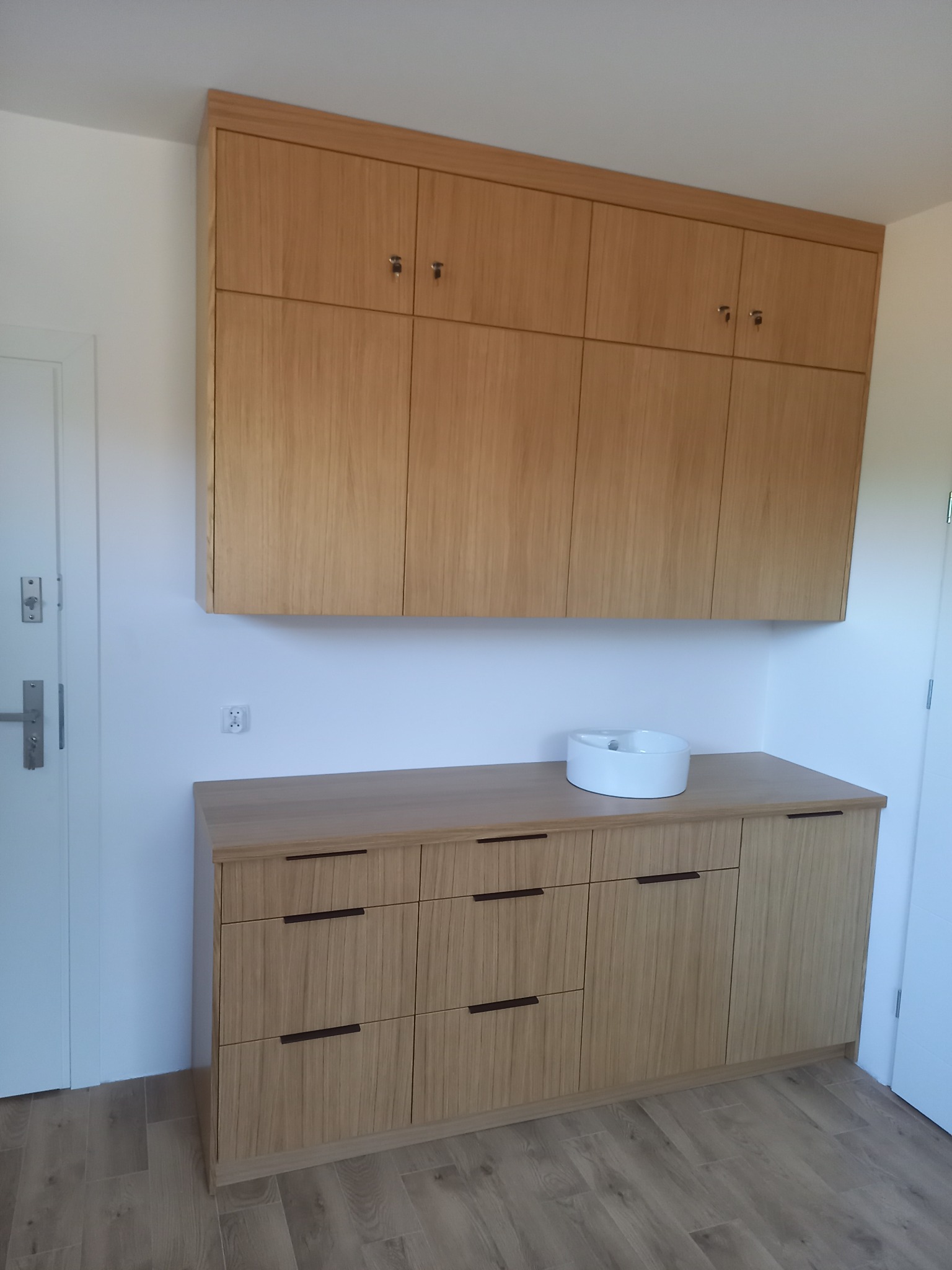 Jasne drewniane szafki wiszące i komoda z umywalką nablatową w Elblągu, minimalistyczny design, widoczne charakterystyczne usłojenie drewna.