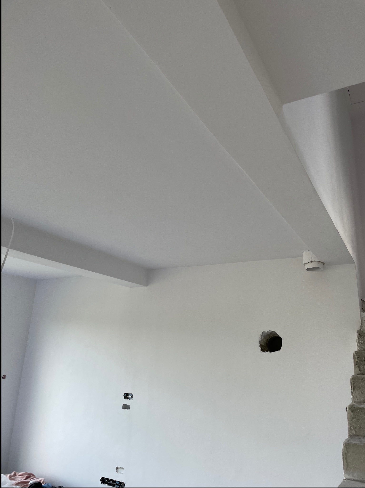 Wnętrze po tynkowaniu: gładkie, białe ściany i sufit z widocznymi elementami konstrukcyjnymi. Otwory na instalacje elektryczne i wentylacyjne. Fragment schodów w prawym rogu.