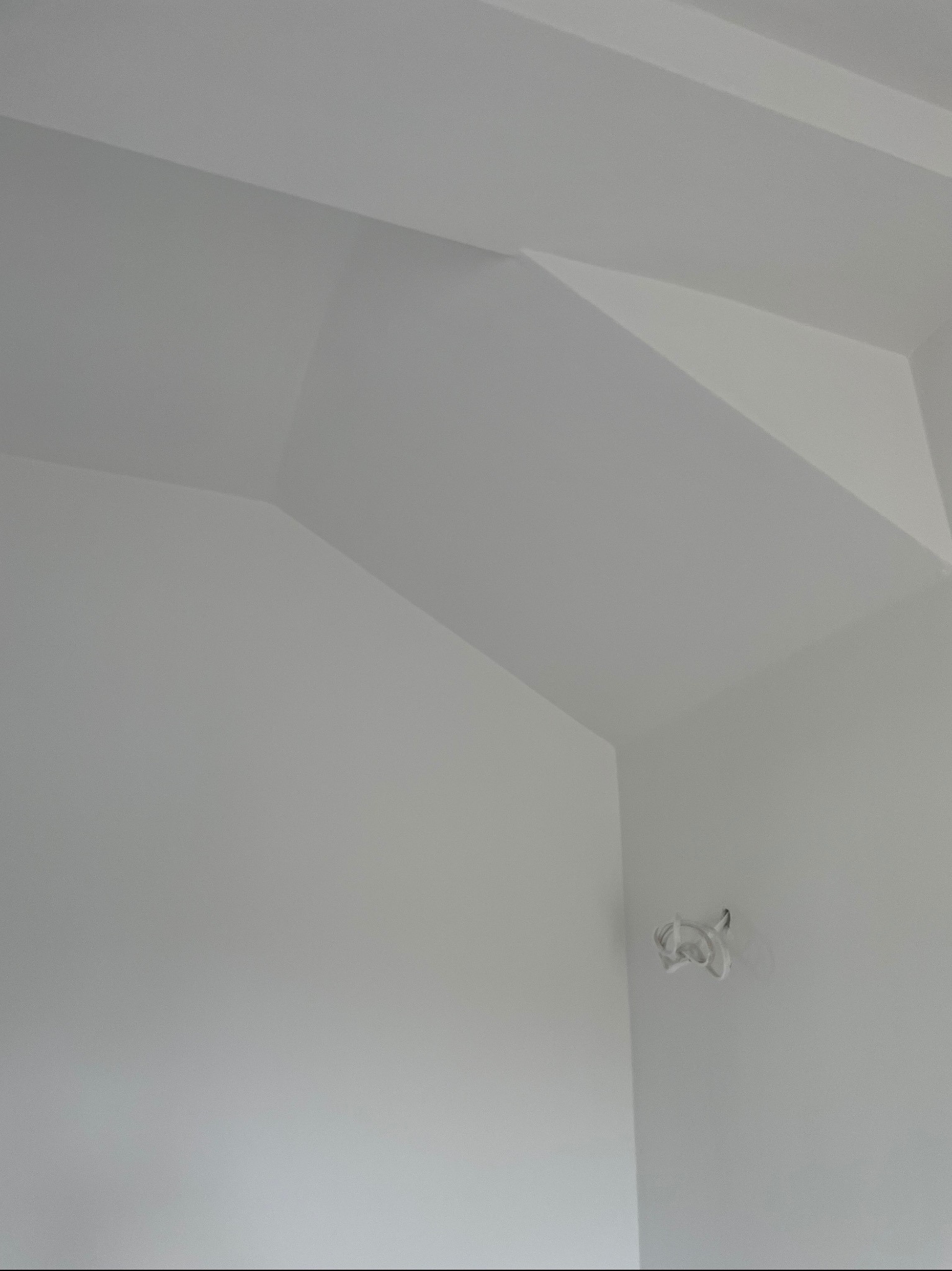 Gładka, biała powierzchnia ściany i sufitu po tynkowaniu maszynowym, z widocznym narożnikiem i wystającym kablem elektrycznym. Minimalistyczne ujęcie.