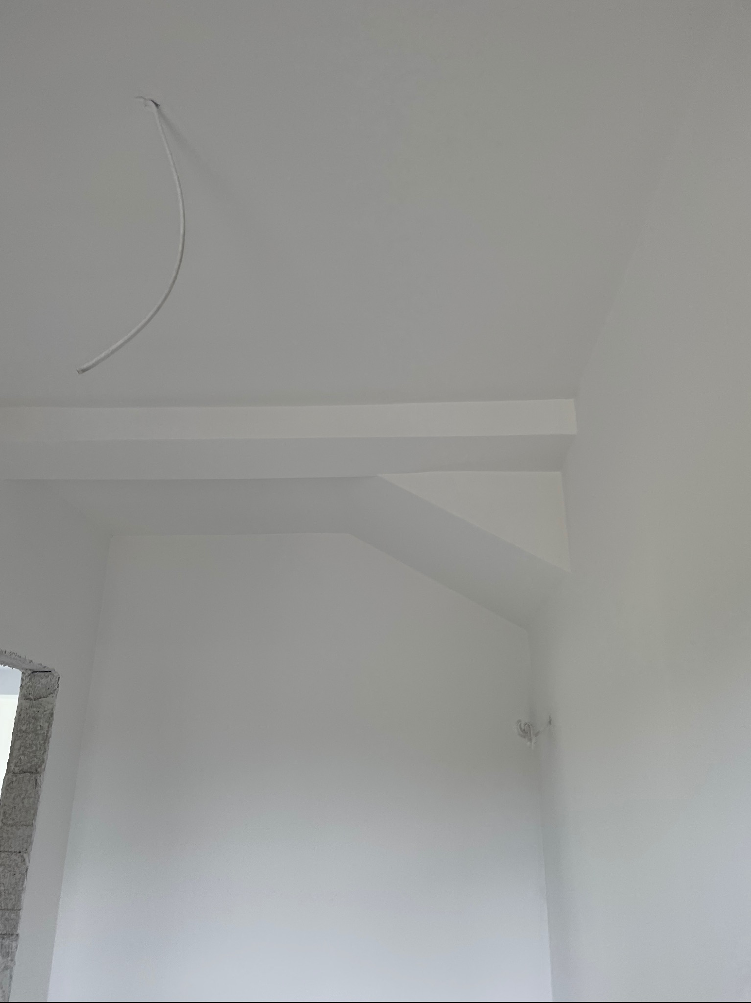 Białe, gładkie ściany i sufit po tynkowaniu maszynowym, widoczny wystający kabel i fragment okna w surowym stanie. Minimalistyczne wnętrze po remoncie.