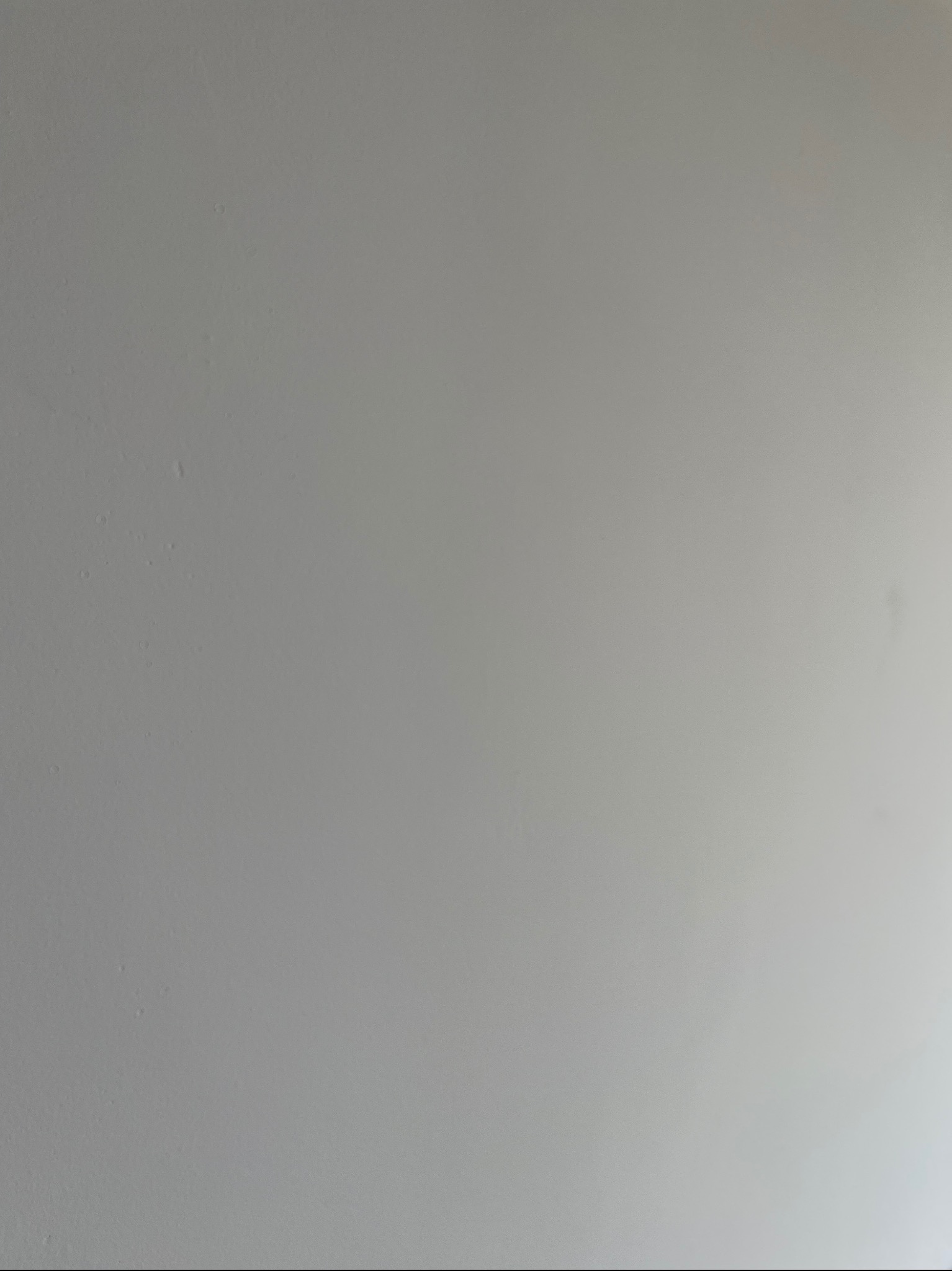 Gładka, szara ściana po tynkowaniu maszynowym, z delikatnym gradientem światła po prawej stronie. Minimalistyczne ujęcie, brak widocznych detali struktury tynku.