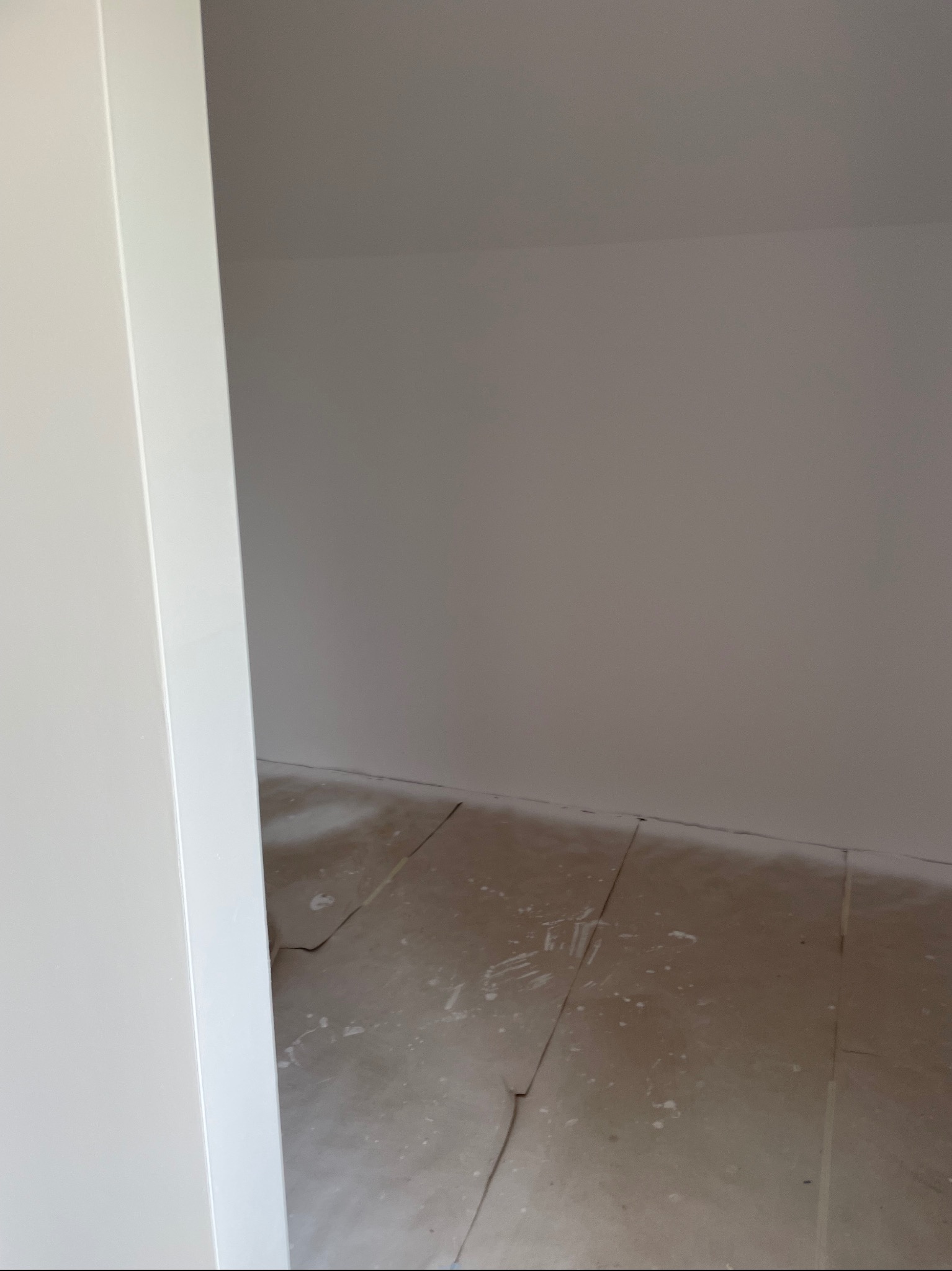 Wnętrze po tynkowaniu: gładkie, szare ściany i podłoga z resztkami zaprawy. Widoczny fragment białej futryny drzwiowej. Minimalistyczne ujęcie, surowe wykończenie.