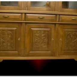 Drewniany kredens z trzema szufladami i trzema szafkami, zdobiony rzeźbionymi ornamentami kwiatowymi i sercowymi na frontach szafek, wykończony w ciepłym, miodowym odcieniu.