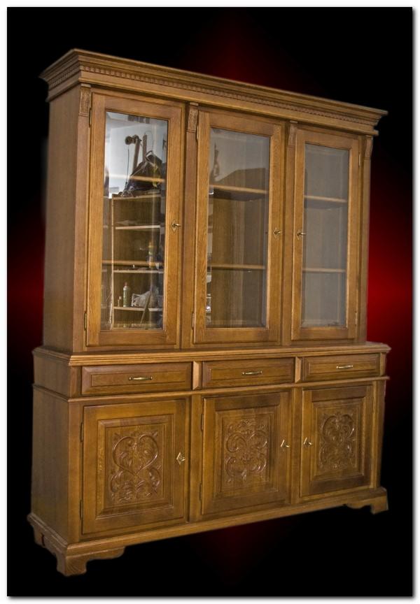 Trzydrzwiowy, dębowy kredens z przeszkloną nadstawką i rzeźbionymi drzwiami, widoczne wnętrze z półkami, oświetlenie studyjne.