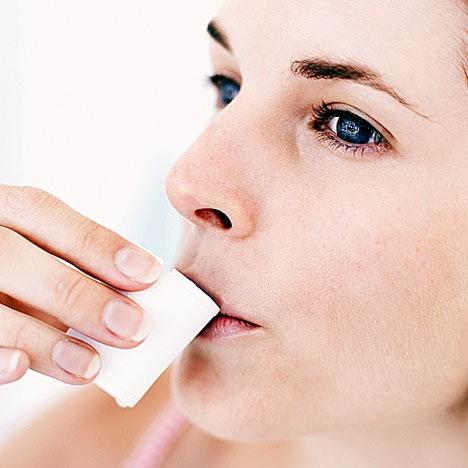 Kobieta przykłada biały, kwadratowy wacik do ust, profil twarzy, jasne tło.