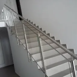 Schody wyłożone płytkami z zamontowaną szklaną balustradą ze stalowymi słupkami i poręczą, widok z dołu.