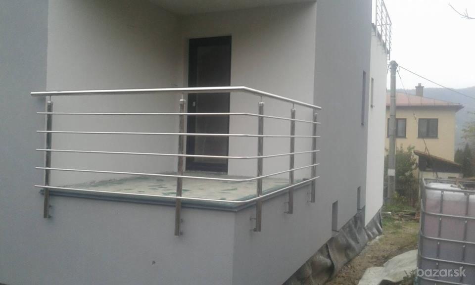 Nowoczesna, metalowa balustrada balkonowa z poziomymi prętami na tle szarej elewacji domu i sąsiedniego budynku.