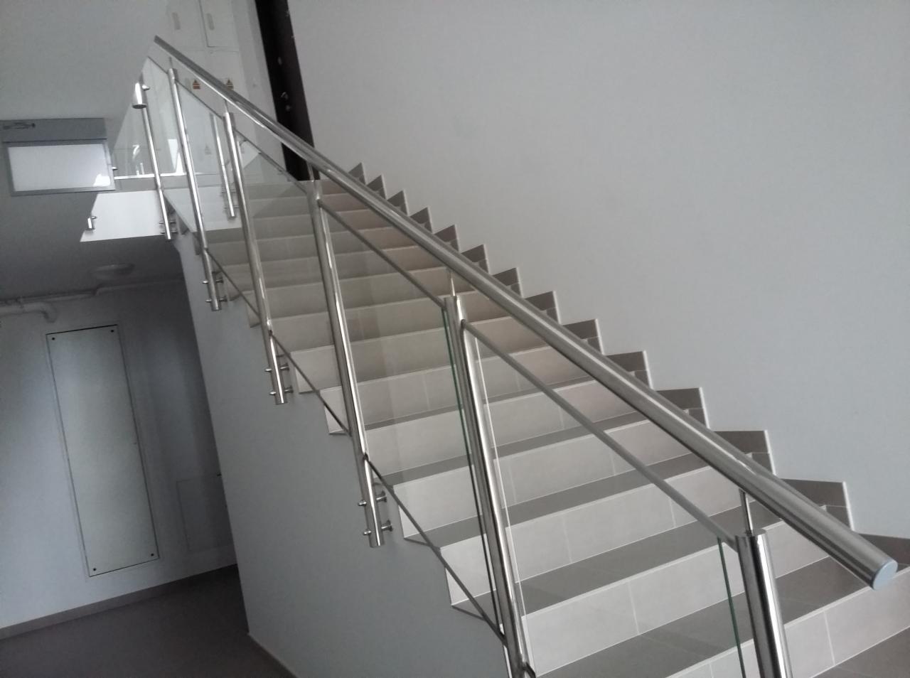 Schody wyłożone płytkami z zamontowaną szklaną balustradą ze stalowymi słupkami i poręczą, widok z dołu.