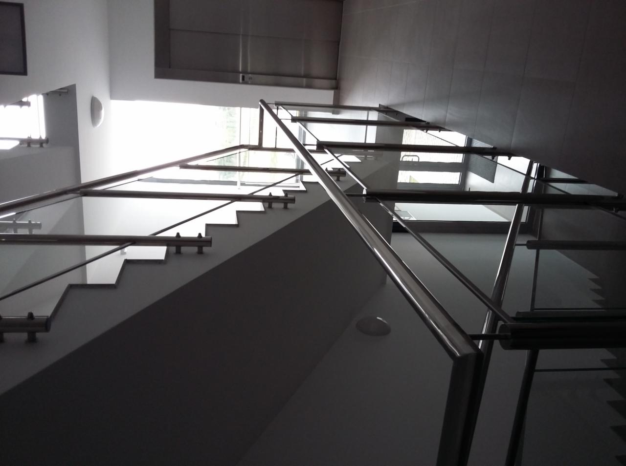 Nowoczesne schody z balustradą nierdzewną i szklanymi panelami, widok z dołu, oświetlenie od góry.