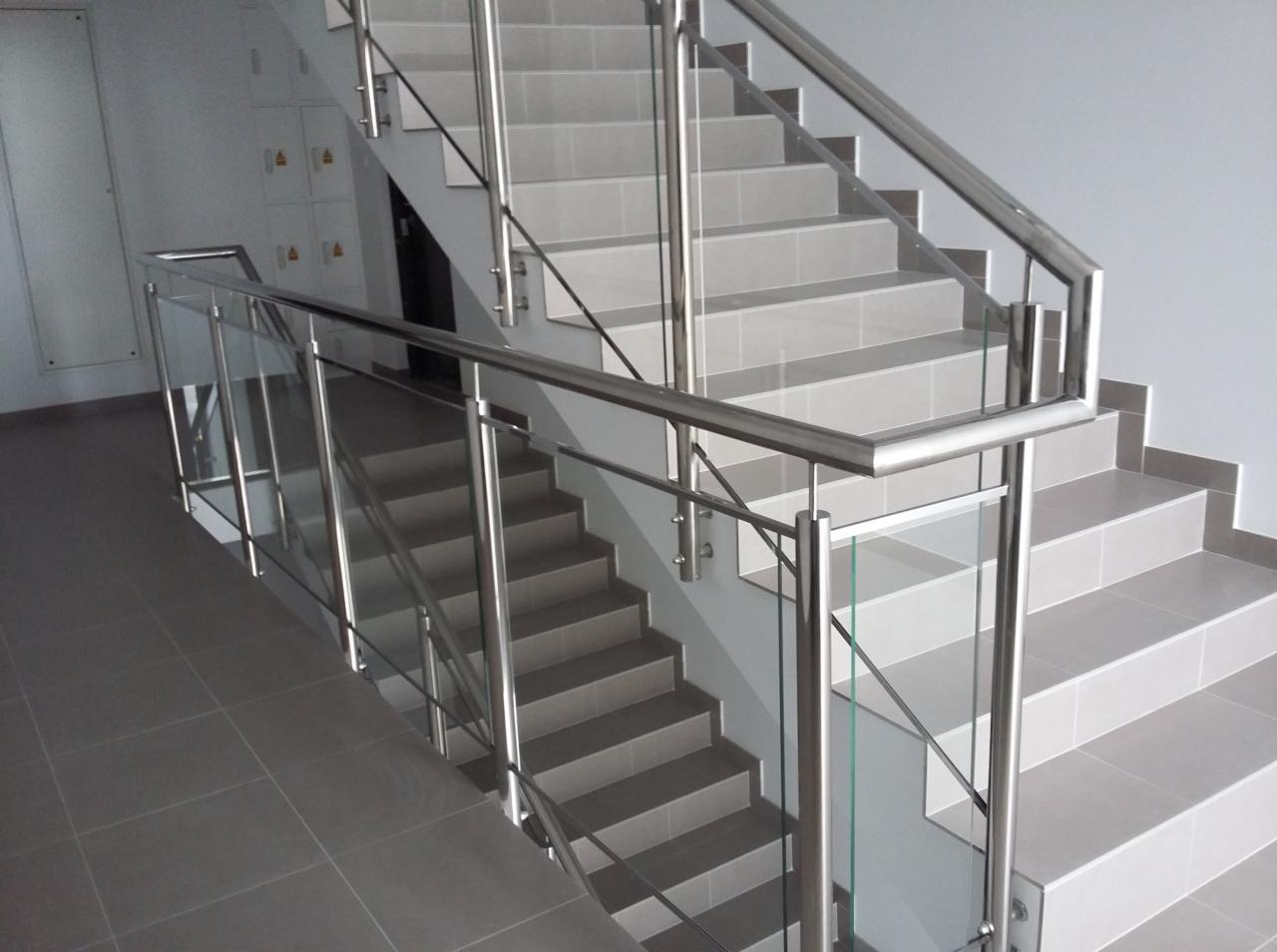 Schody wyłożone szarą płytką z balustradą ze stali nierdzewnej i szkła, widok z dołu.