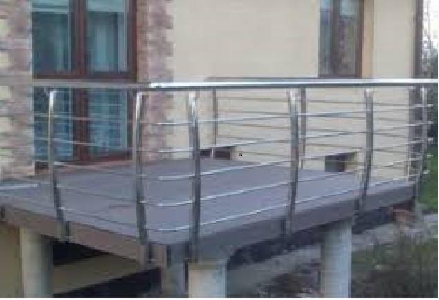 Balkon z podestem wyłożonym szarymi panelami kompozytowymi, zabezpieczony nowoczesną balustradą ze stali nierdzewnej z poziomymi prętami, na tle elewacji budynku z ceglanym fragmentem.