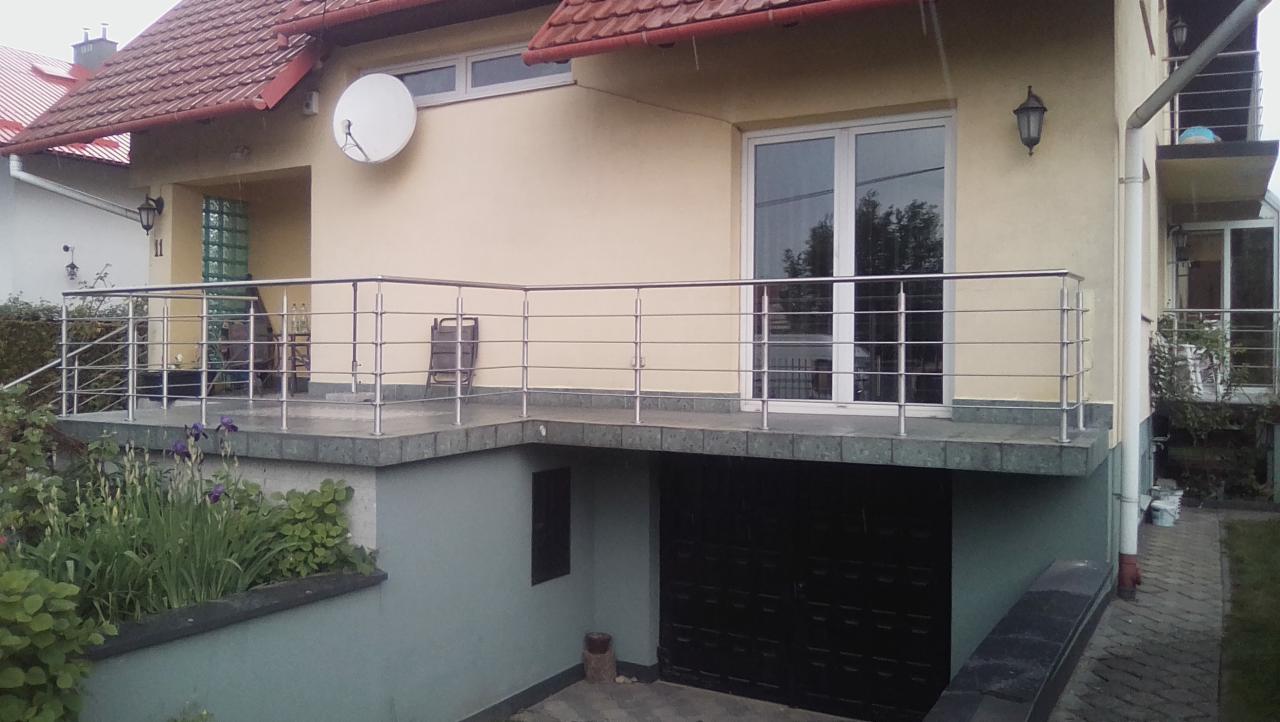 Zewnętrzna, pozioma balustrada ze stali nierdzewnej, zamontowana na betonowym tarasie z wejściem do garażu w piwnicy, widok na część budynku z oknami i satelitą.