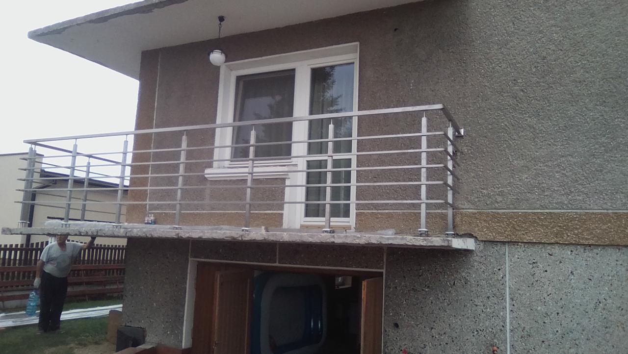 Balkon z nową, poziomą, nierdzewną balustradą, widok z dołu, z fragmentem elewacji budynku i osobą stojącą obok.
