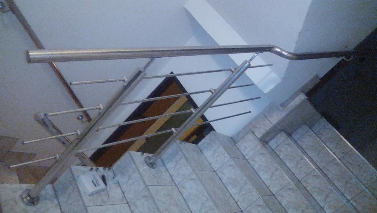 Schody wyłożone jasnymi płytkami z szarą, metalową balustradą z poziomymi poprzeczkami; widok z góry.